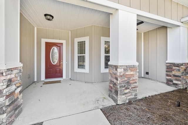 view of exterior entry with covered porch, stone siding, and board and batten siding