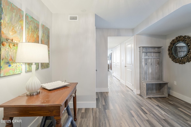 corridor featuring visible vents, baseboards, and wood finished floors