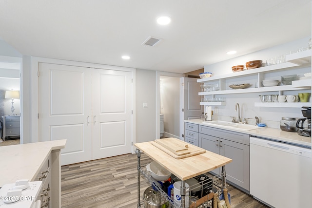 kitchen with visible vents, light wood-style flooring, white dishwasher, open shelves, and a sink