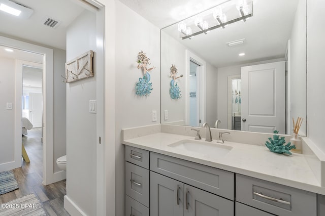 ensuite bathroom featuring toilet, baseboards, wood finished floors, and vanity