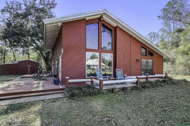 rear view of property with an outbuilding, a storage unit, a deck, and a yard