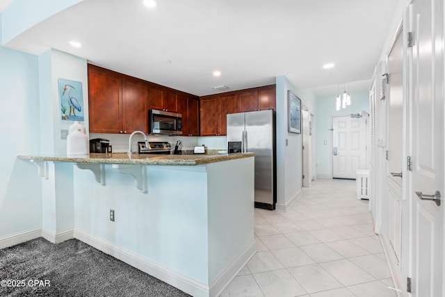kitchen with a breakfast bar, light stone counters, recessed lighting, appliances with stainless steel finishes, and a peninsula