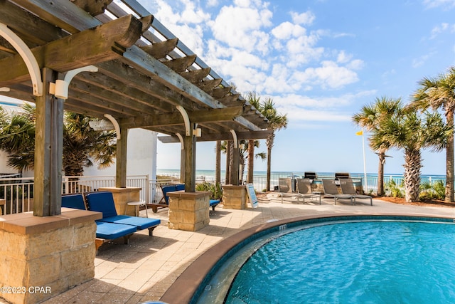 pool with exterior kitchen, a patio area, a pergola, and a water view
