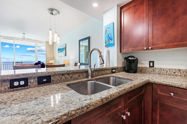 kitchen with hanging light fixtures, light stone counters, dark brown cabinets, and a sink