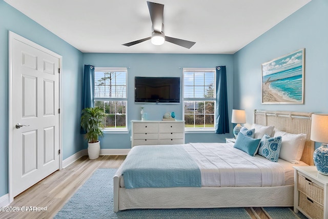 bedroom featuring light wood finished floors, multiple windows, a ceiling fan, and baseboards