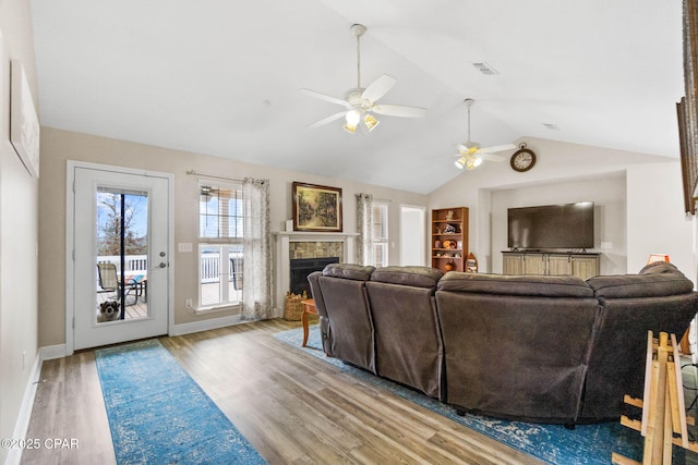 living room with baseboards, visible vents, a tiled fireplace, vaulted ceiling, and light wood-style floors