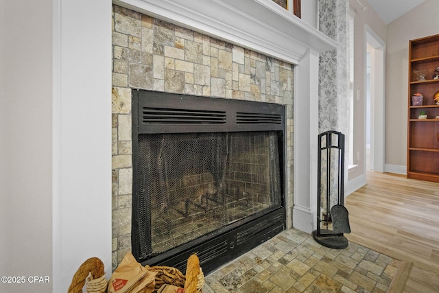 details featuring a stone fireplace, baseboards, and wood finished floors