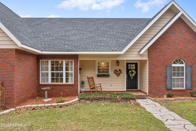 entrance to property with a shingled roof, brick siding, and a yard