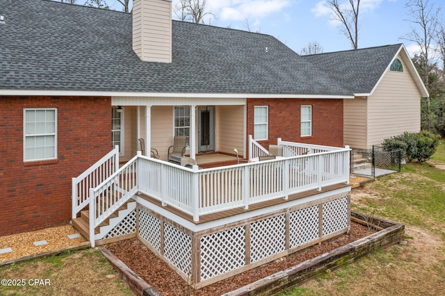 rear view of house with a shingled roof, a chimney, a porch, and brick siding