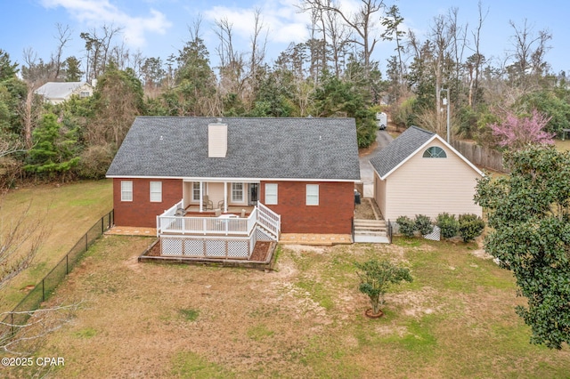 rear view of property featuring brick siding, a wooden deck, a chimney, and a yard