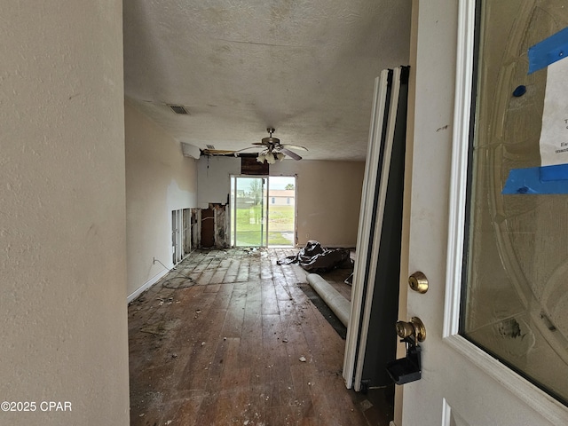 unfurnished living room featuring hardwood / wood-style flooring, visible vents, a ceiling fan, and a textured wall