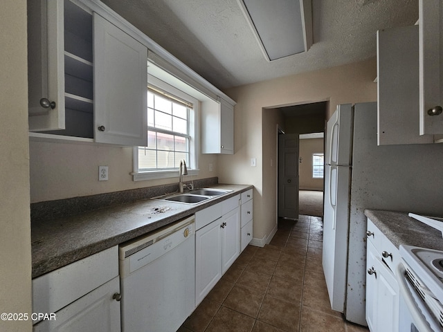 kitchen featuring dark countertops, white cabinetry, a sink, dark tile patterned flooring, and white appliances