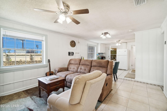 living area with visible vents, a textured ceiling, crown molding, light tile patterned floors, and ceiling fan