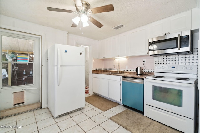 kitchen with white appliances, light tile patterned floors, visible vents, a sink, and white cabinetry