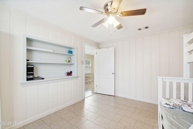 interior space with visible vents, a ceiling fan, a textured ceiling, a decorative wall, and light tile patterned floors