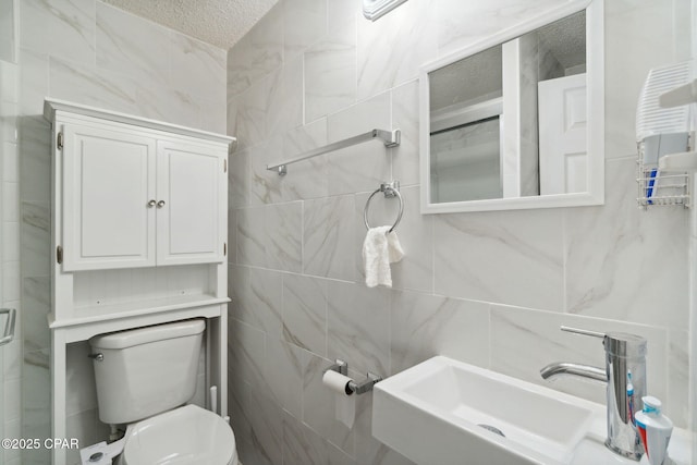 bathroom with tile walls, toilet, a shower with shower door, a textured ceiling, and a sink