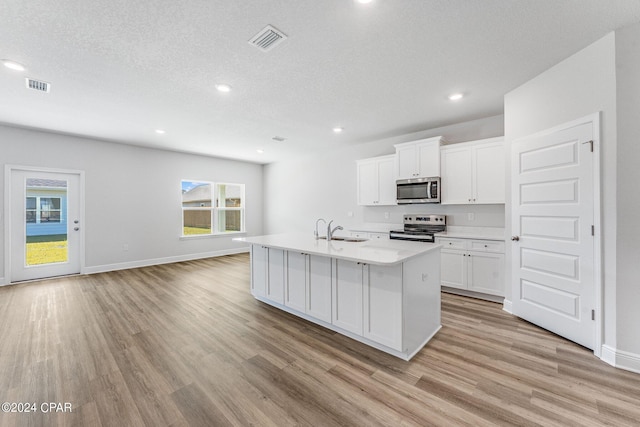 kitchen with light countertops, appliances with stainless steel finishes, a center island with sink, and white cabinetry