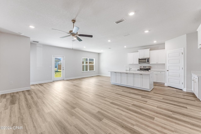 kitchen featuring white cabinets, open floor plan, stainless steel appliances, light countertops, and a sink