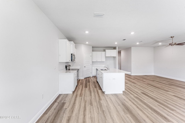 kitchen with a center island with sink, light countertops, appliances with stainless steel finishes, open floor plan, and white cabinets