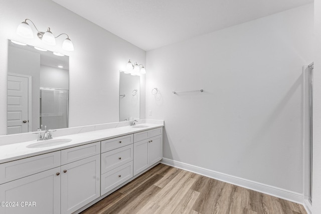 full bathroom with wood finished floors, a sink, a shower with shower door, and baseboards