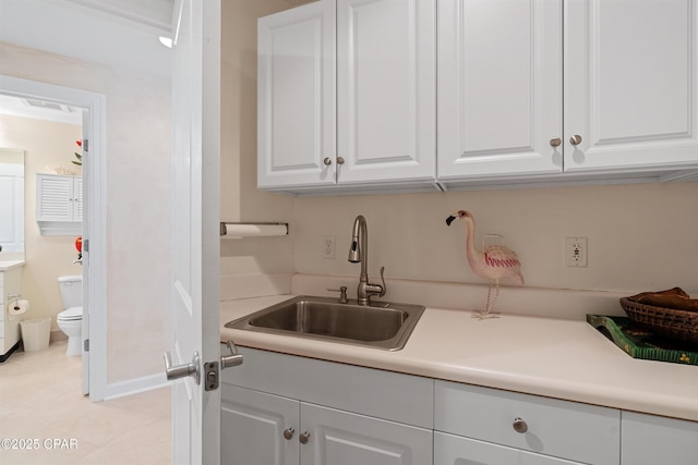 kitchen featuring light countertops, white cabinets, a sink, and baseboards