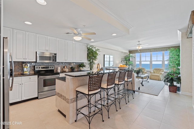 kitchen featuring a breakfast bar, crown molding, stainless steel appliances, tasteful backsplash, and open floor plan