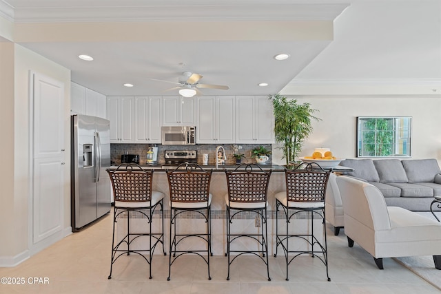 kitchen with stainless steel appliances, dark countertops, a kitchen bar, and white cabinets