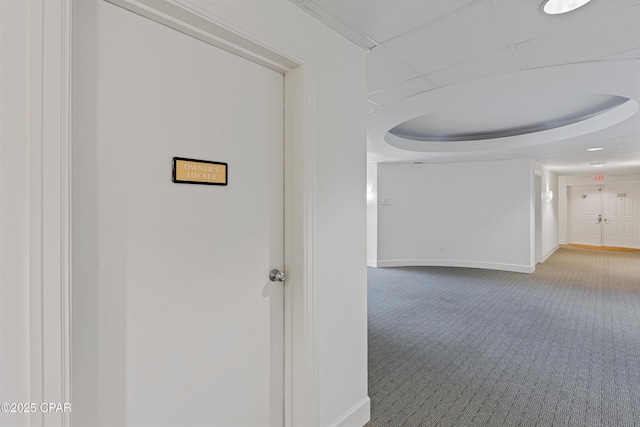 hallway with baseboards, a raised ceiling, and carpet flooring