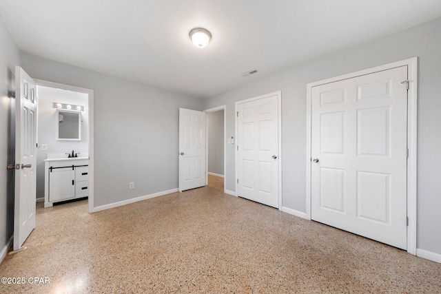 unfurnished bedroom featuring baseboards, visible vents, ensuite bathroom, and light speckled floor