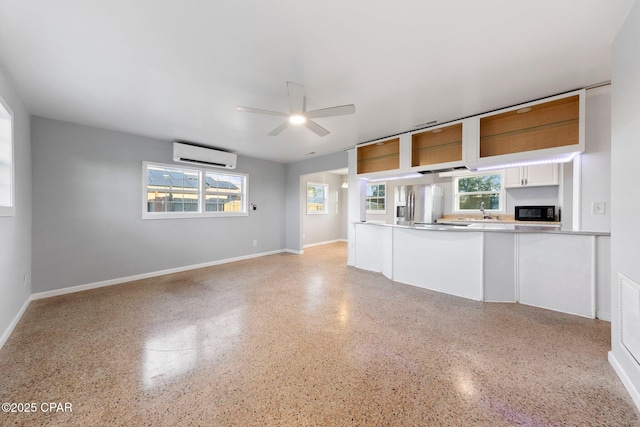unfurnished living room featuring an AC wall unit, ceiling fan, a sink, and a wealth of natural light