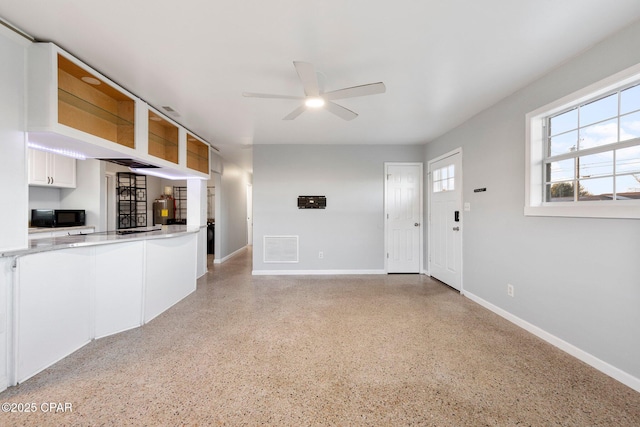 unfurnished living room with baseboards, a ceiling fan, visible vents, and light speckled floor