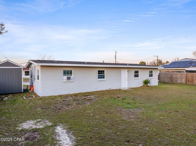 rear view of house with a lawn, fence, an outdoor structure, a shed, and concrete block siding