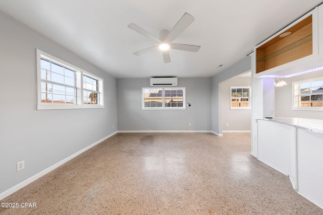 unfurnished living room featuring baseboards, a wall mounted air conditioner, ceiling fan, and light speckled floor
