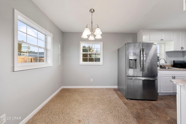 kitchen with a sink, light countertops, white cabinetry, baseboards, and stainless steel refrigerator with ice dispenser