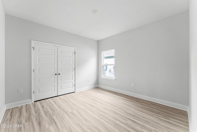 unfurnished bedroom featuring light wood-style floors, baseboards, and a closet