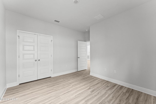 unfurnished bedroom featuring light wood-type flooring, baseboards, visible vents, and a closet