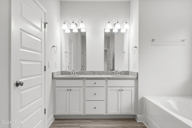 full bath with double vanity, wood finished floors, a sink, and a bath