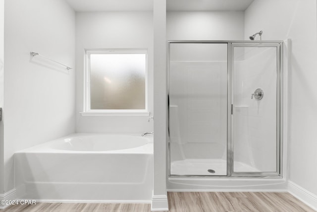 full bath featuring a stall shower, a bath, baseboards, and wood finished floors