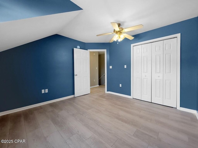 unfurnished bedroom with lofted ceiling, a closet, a ceiling fan, wood finished floors, and baseboards