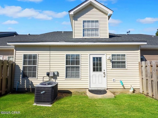 back of house with roof with shingles, central AC unit, a lawn, and fence