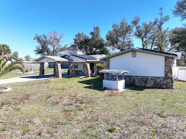 rear view of house featuring stone siding, a yard, and fence