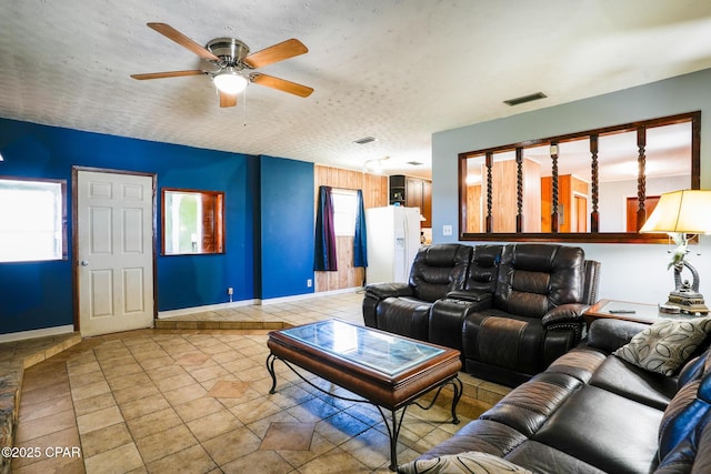 living area with a textured ceiling, ceiling fan, visible vents, and baseboards