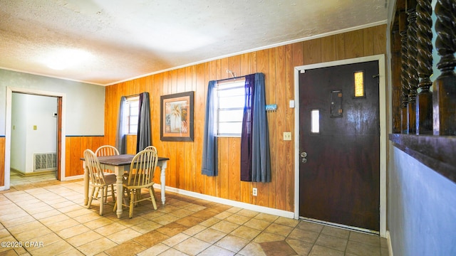 dining room with visible vents, ornamental molding, light tile patterned flooring, a textured ceiling, and wooden walls