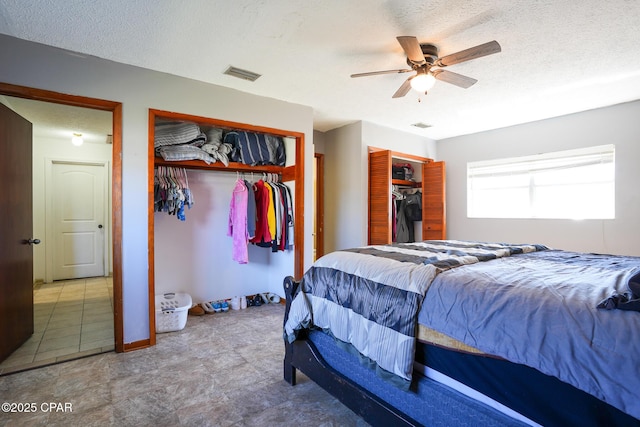 bedroom with two closets, ceiling fan, visible vents, and a textured ceiling