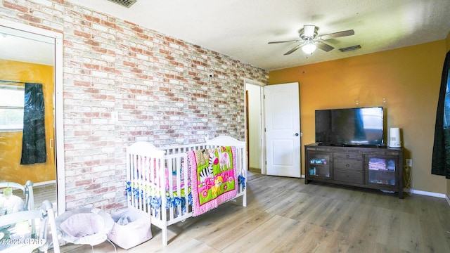 bedroom featuring brick wall, visible vents, baseboards, and wood finished floors