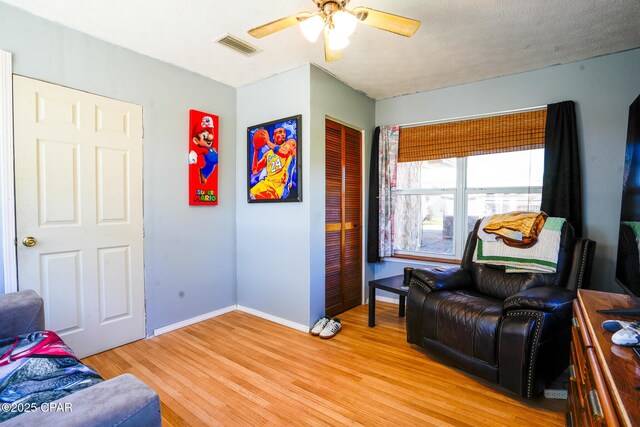 sitting room with visible vents, light wood-style floors, a ceiling fan, a textured ceiling, and baseboards