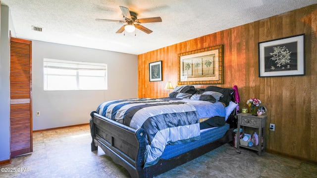 bedroom featuring visible vents, a ceiling fan, wooden walls, a textured ceiling, and baseboards
