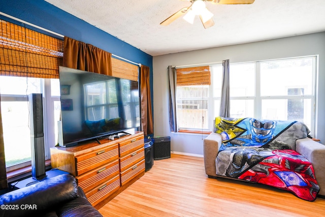 living room with a textured ceiling, light wood-type flooring, a ceiling fan, and baseboards