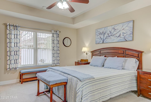 bedroom featuring light carpet, a tray ceiling, baseboards, and a ceiling fan