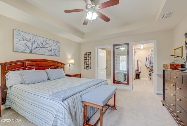 bedroom with a spacious closet, a tray ceiling, visible vents, and light colored carpet